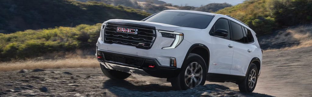 A white GMC Acadia AT4 driving off-road in a rugged terrain.