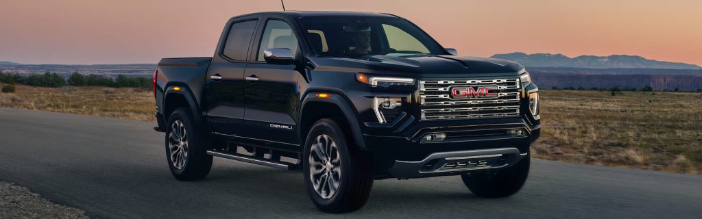A black GMC Canyon Denali driving on a rural road with mountains in the background.