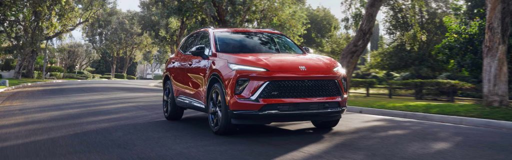 A red Buick Envision driving on a tree-lined street.