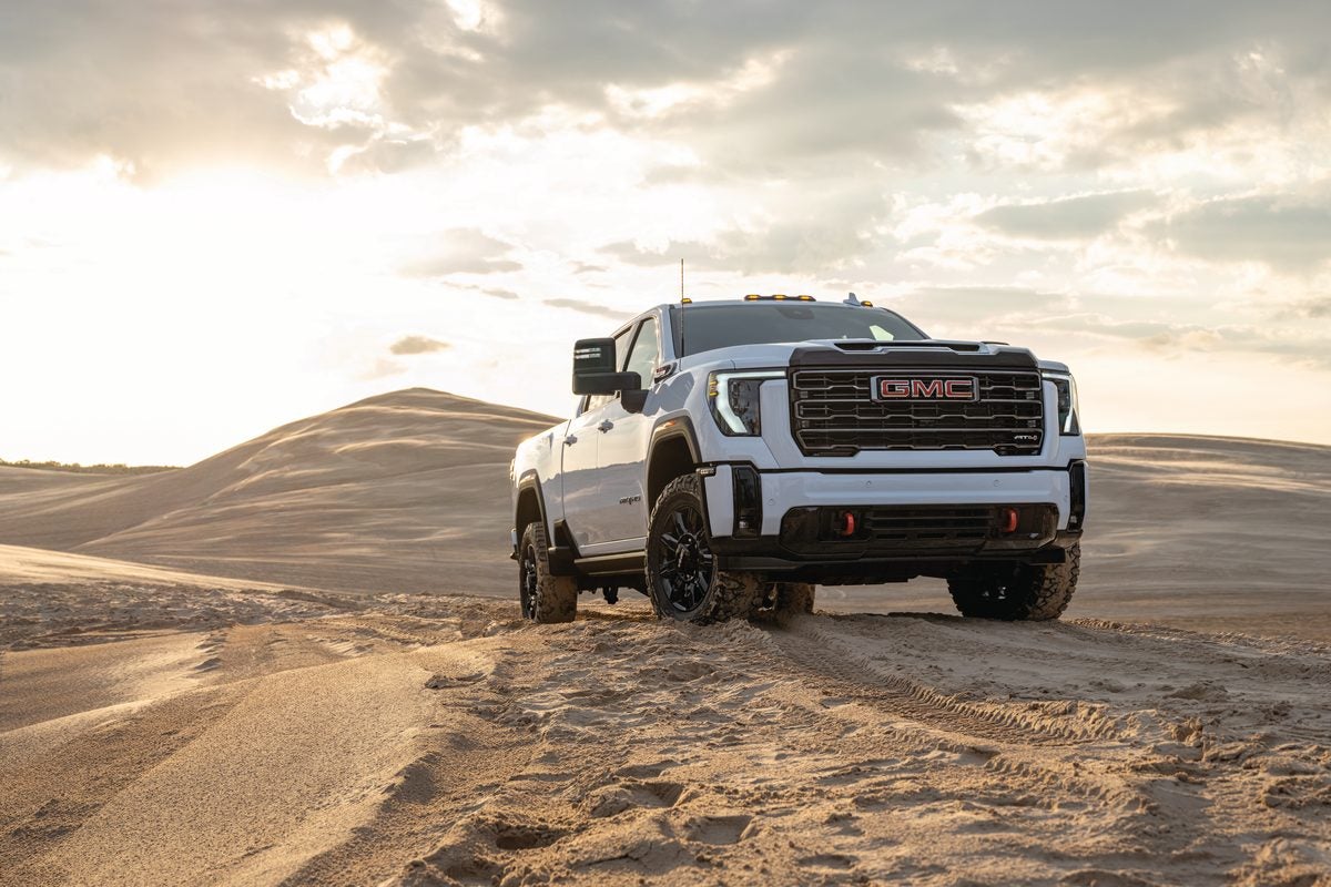 White GMC Sierra HD AT4 climbing a sand dune under a bright sky