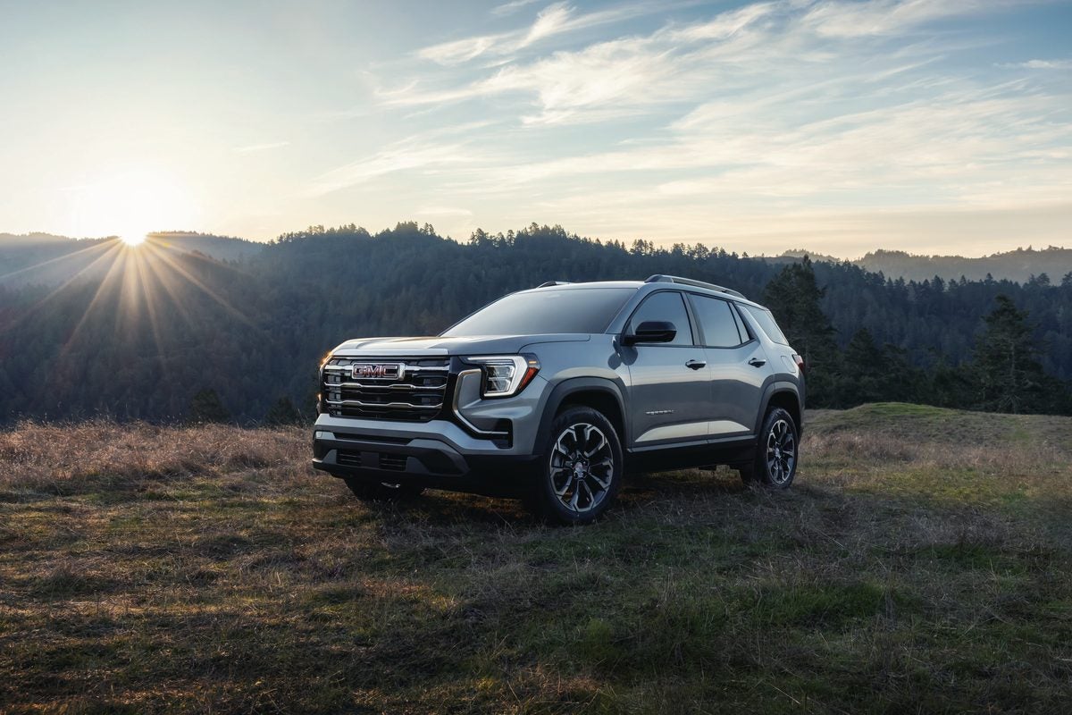 Silver GMC Terrain AT4 on a grassy hilltop with the sun rising over wooded hills