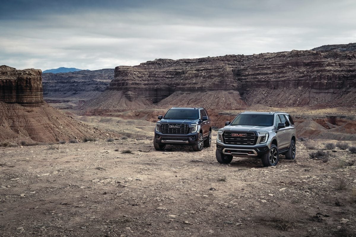 Two 2027 GMC Yukon SUVs parked on a desert mesa with canyon walls behind