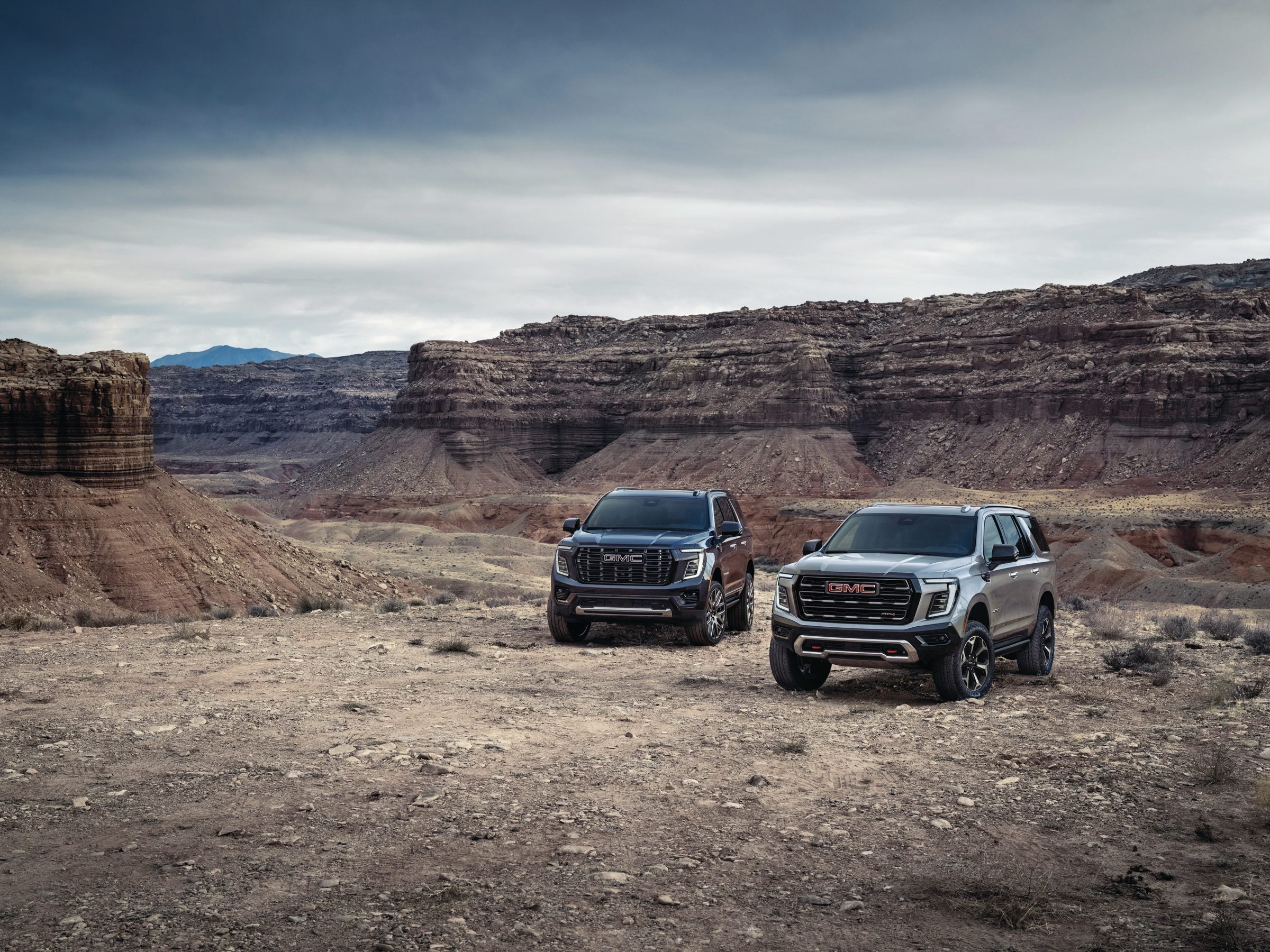 Two 2027 GMC Yukon SUVs, an AT4 and a Denali, parked on a desert mesa