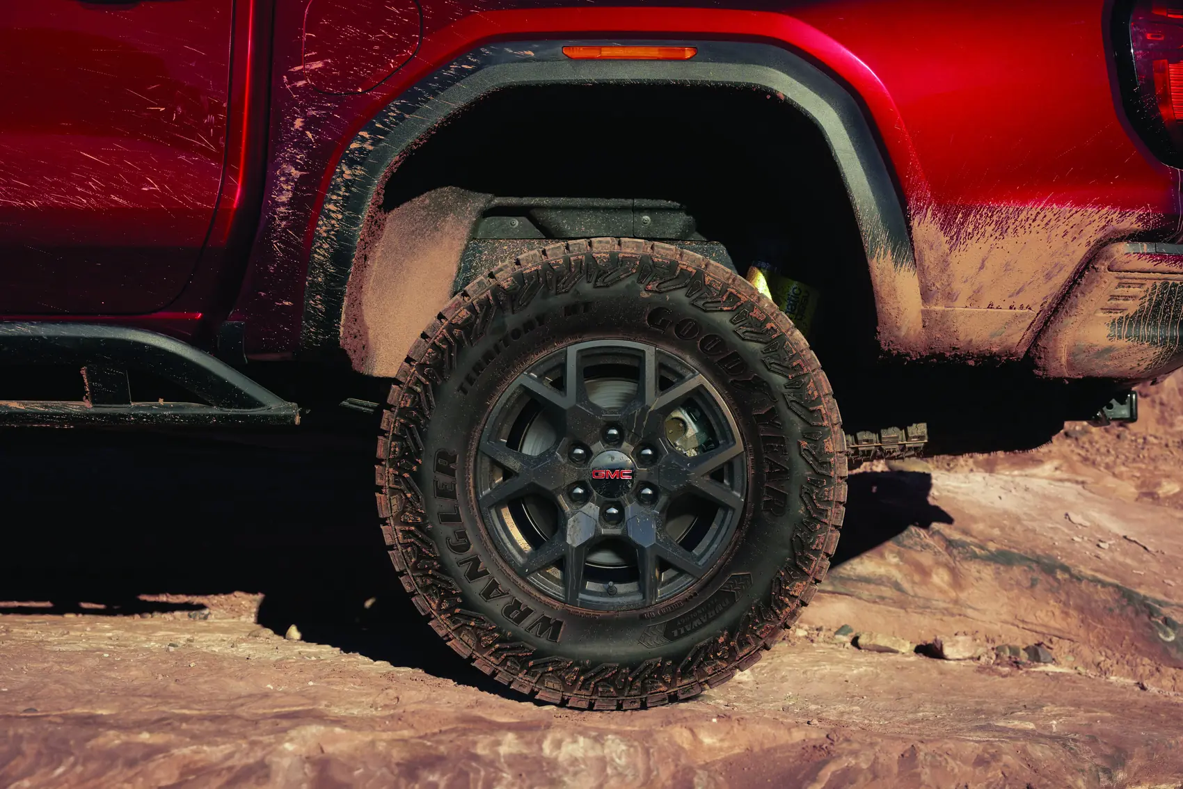 2027 GMC Canyon AT4 17 inch wheel in Volcanic Red Tintcoat on a rock trail