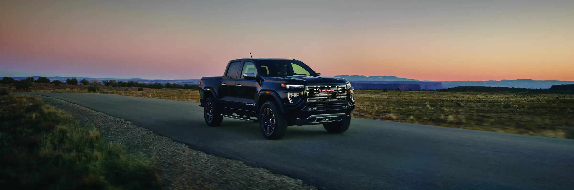 2027 GMC Canyon Denali in Onyx Black on an open road at dusk