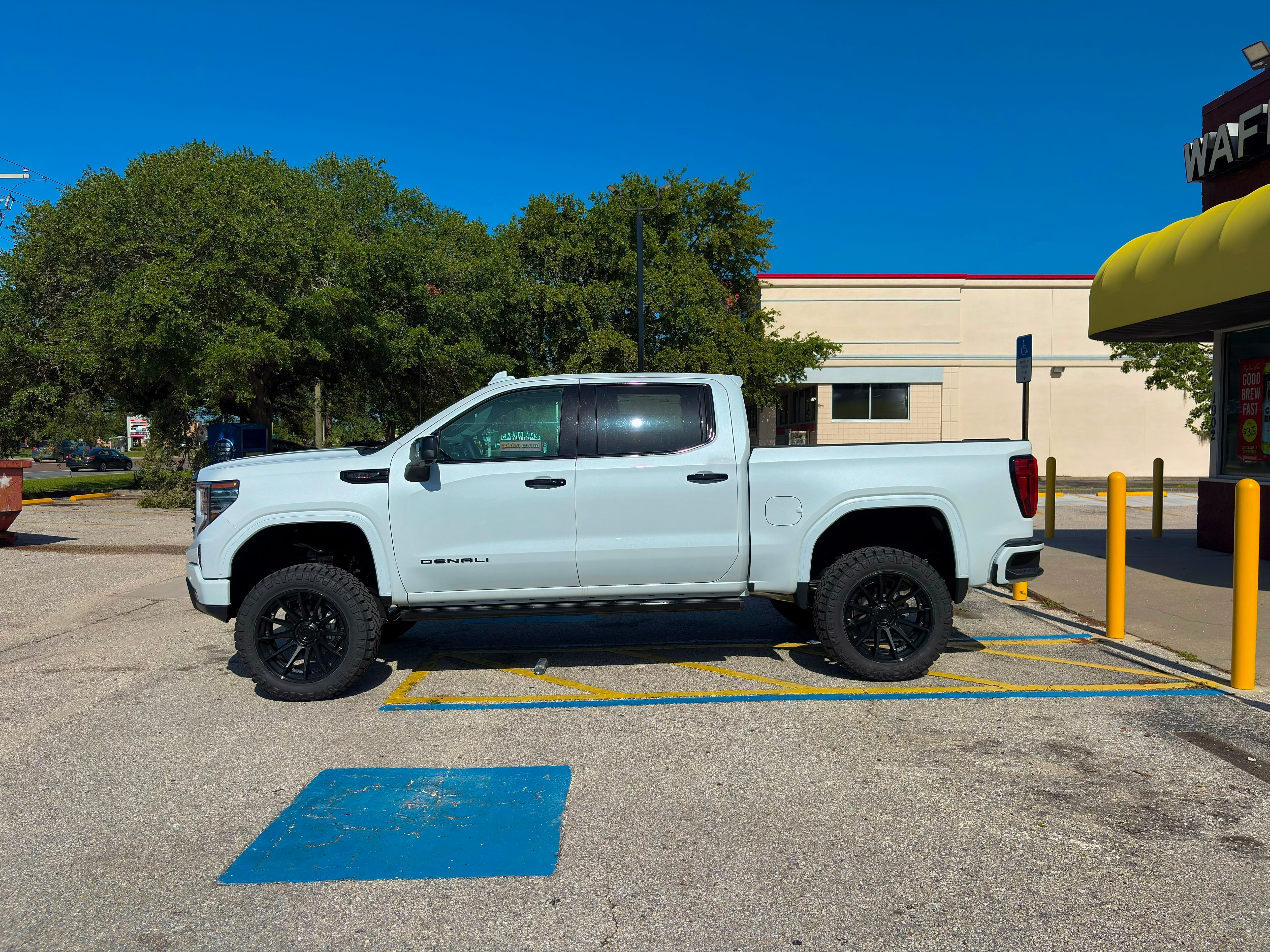 Side profile of a lifted white GMC Sierra 1500 Denali on black wheels