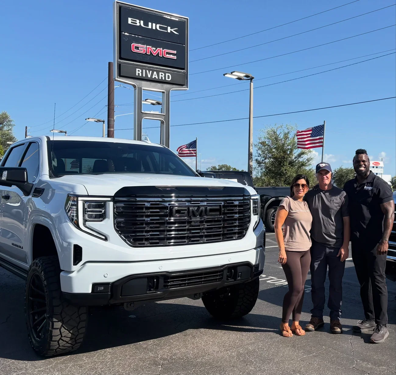 The Newman family with their custom lifted white Sierra 1500 Denali under the Rivard Buick GMC sign